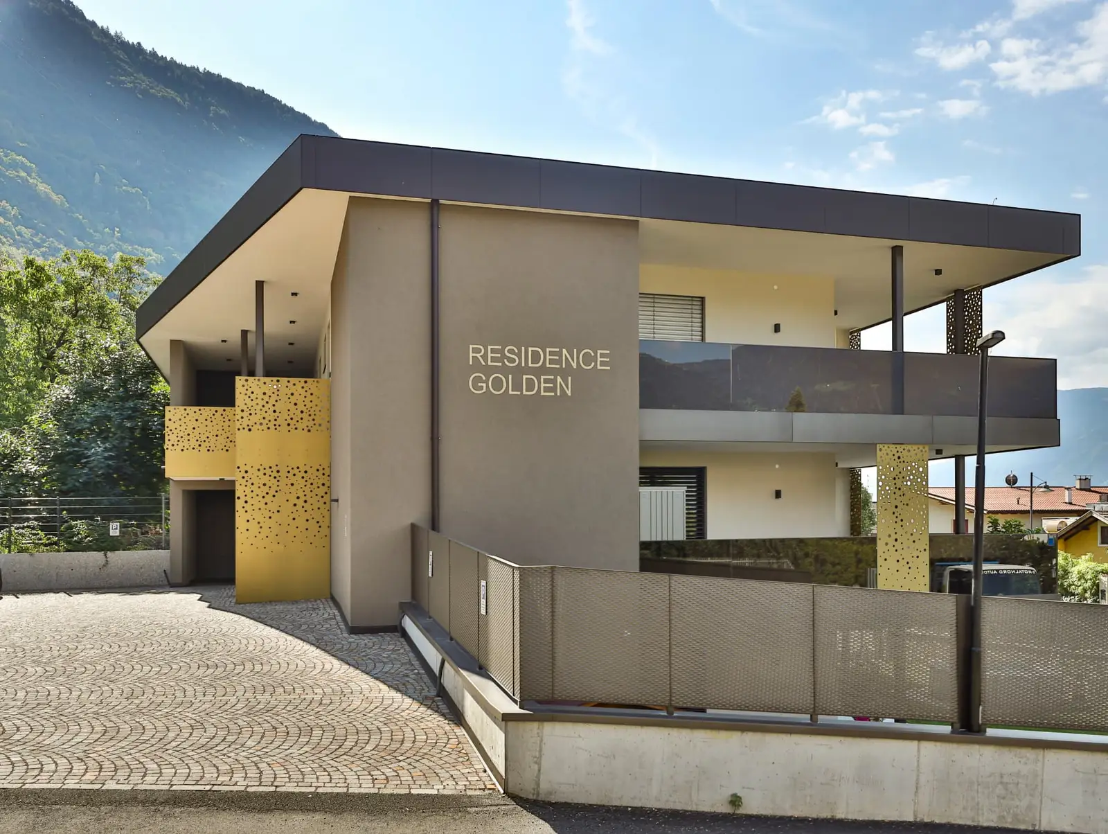 Residence Golden Burgstall — Eingangsfassade mit Schriftzug und goldenen Lochblech-Elementen