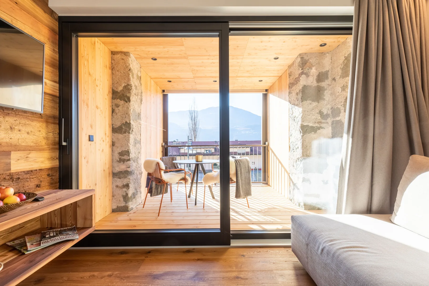 Wohnzimmer mit Altholzwand und geöffneter Schiebetür zur Loggia mit Bergblick