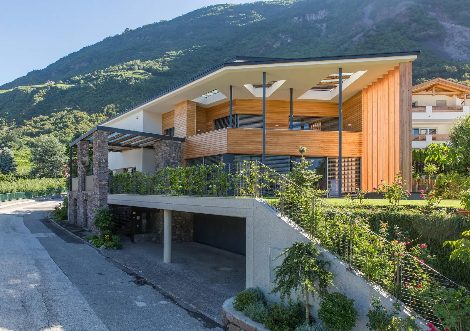 Villa P Burgstall — Straßenansicht mit Holzfassade, Pergola aus Naturstein und Garage