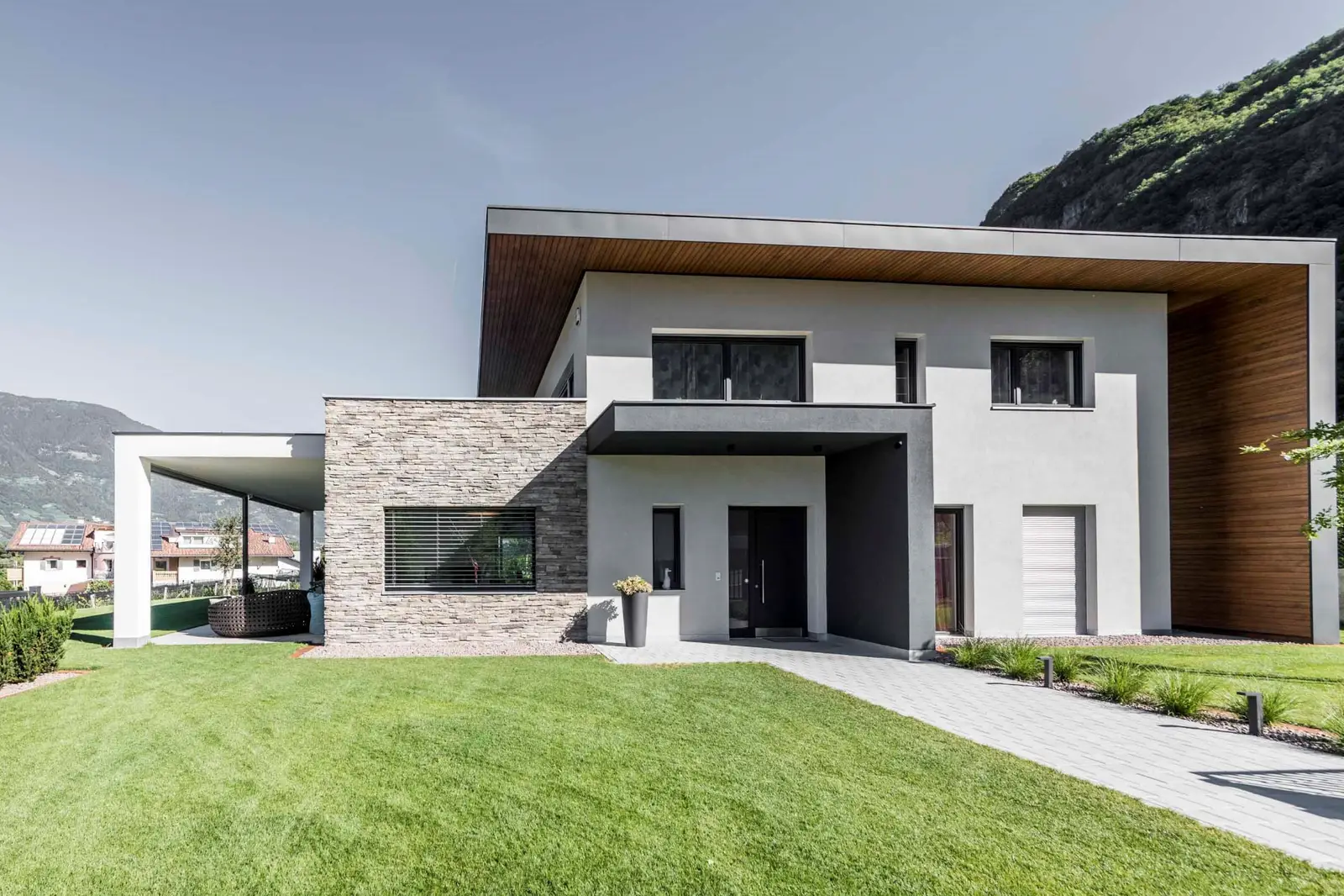 Villa V Burgstall — Straßenansicht mit Natursteinfassade, Holzuntersicht und überdachtem Eingang